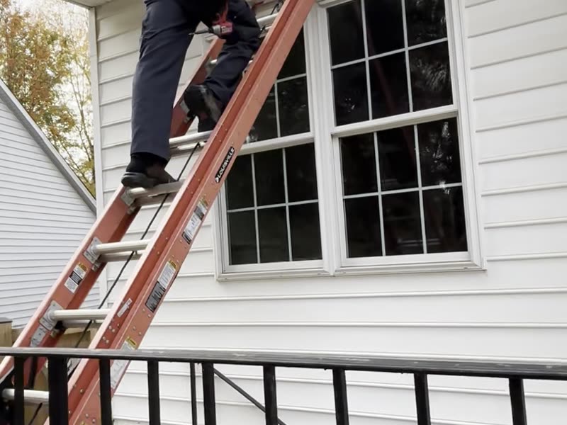 Working from a ladder at the roofline of a vacant house
